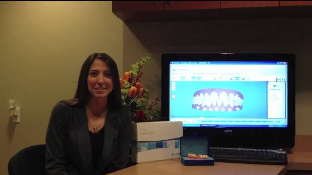 Woman smiling beside computer screen displaying 3D Invisalign treatment plan and aligners.